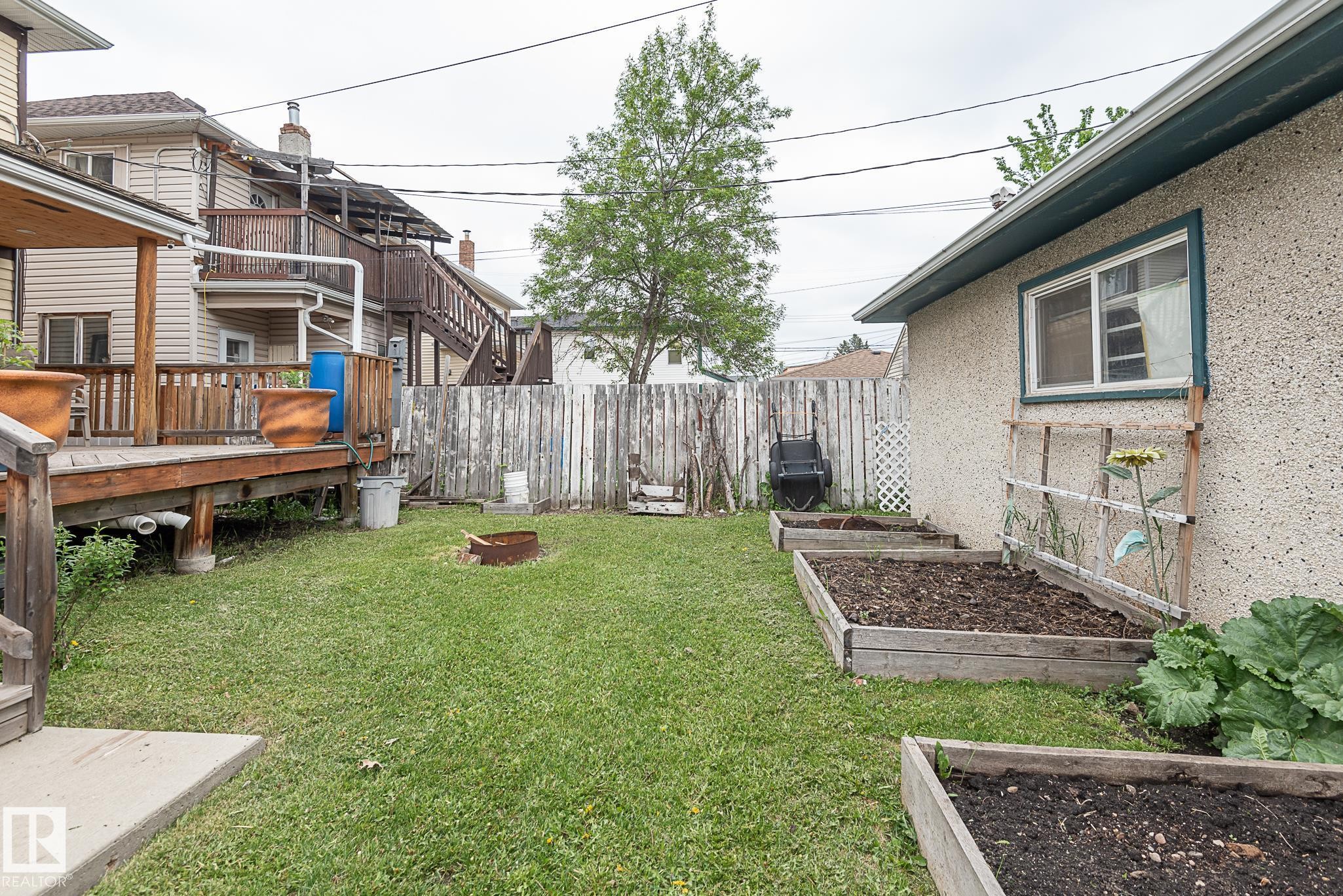 Expansive backyard featuring a manicured lawn, a raised wood deck, and multiple raised garden beds - 9623 110A Avenue, Edmonton, AB