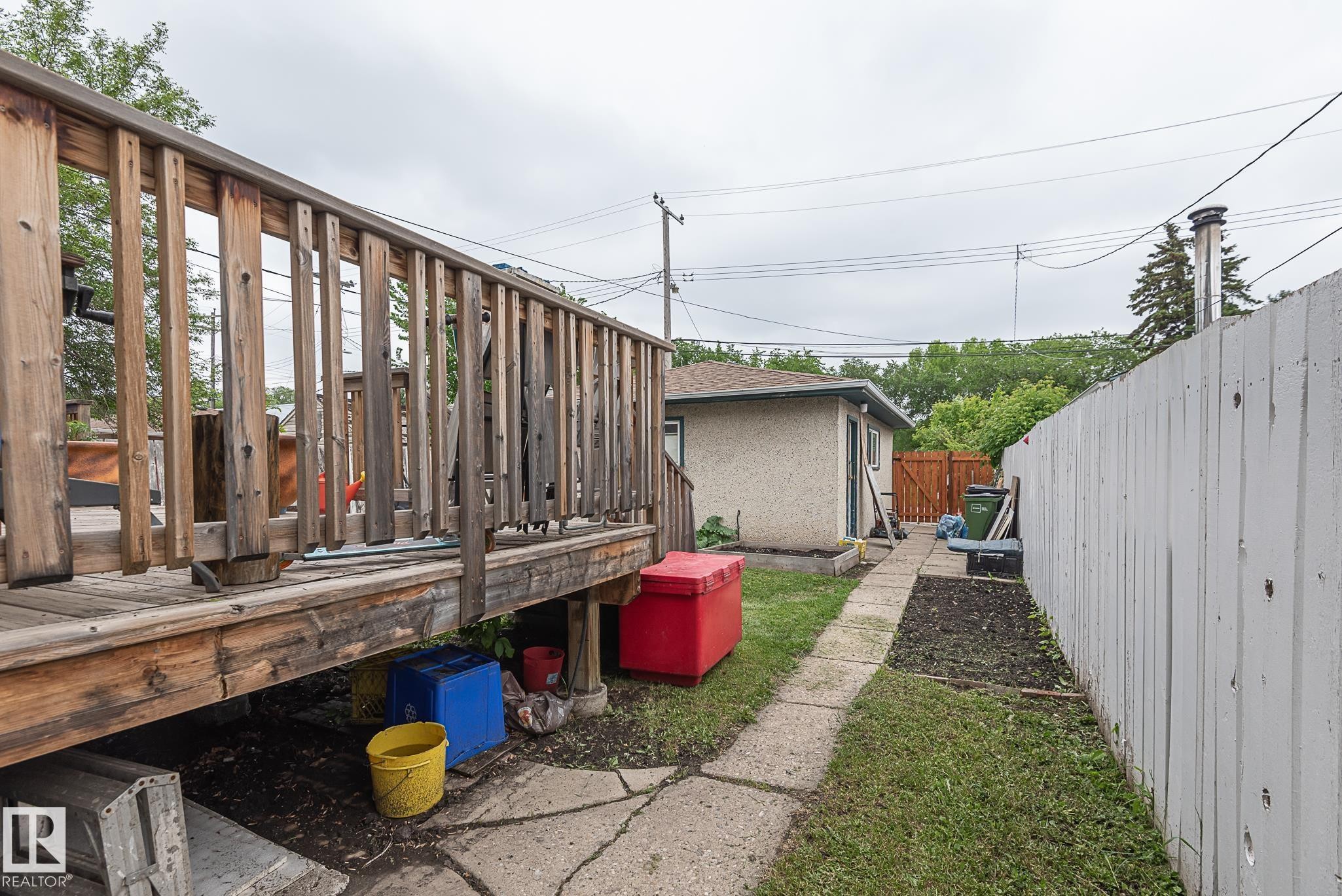 Expansive wooden deck with a privacy fence and a concrete pathway leading to an outbuilding with stucco siding - 9623 110A Avenue, Edmonton, AB