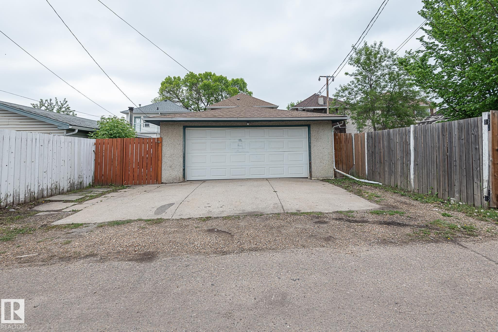 Detached garage featuring a white sectional door, stucco exterior, asphalt shingle roof, and concrete driveway - 9623 110A Avenue, Edmonton, AB