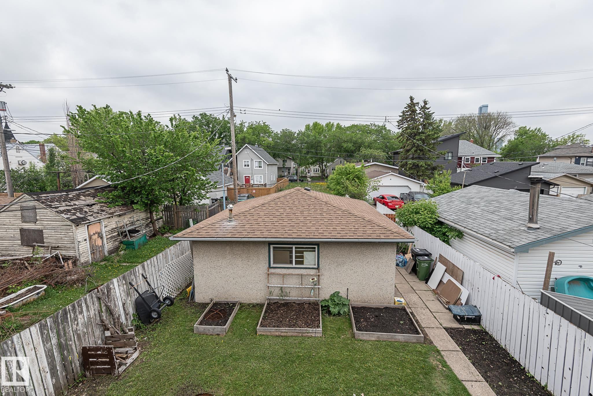 Expansive backyard featuring a manicured lawn, three raised garden beds, and a concrete paver pathway - 9623 110A Avenue, Edmonton, AB