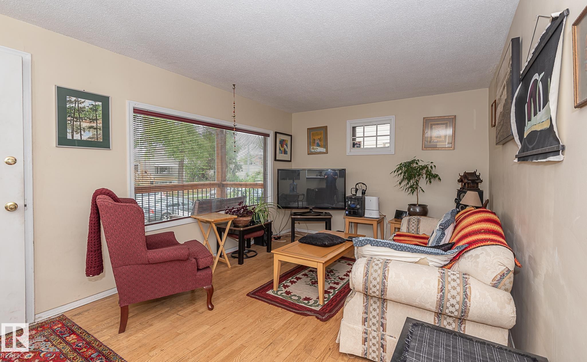 Living area featuring wood-finish flooring, light-toned walls, a large picture window with blinds, and a secondary transom window - 9623 110A Avenue, Edmonton, AB