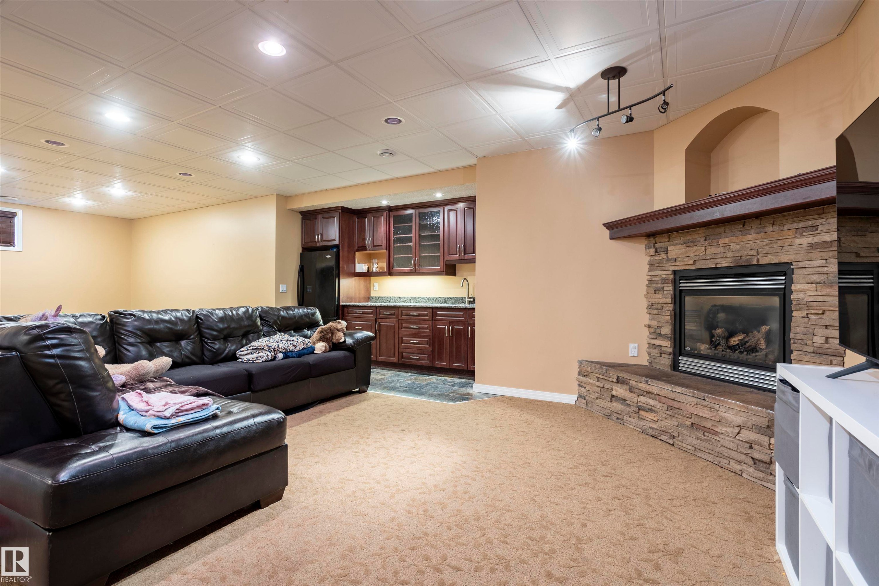 Living area featuring a stacked stone fireplace with a wood mantel, recessed lighting, drop ceiling, and a wet bar with dark wood cabinetry and a countertop - 1441 Highwood Boulevard, Devon, AB