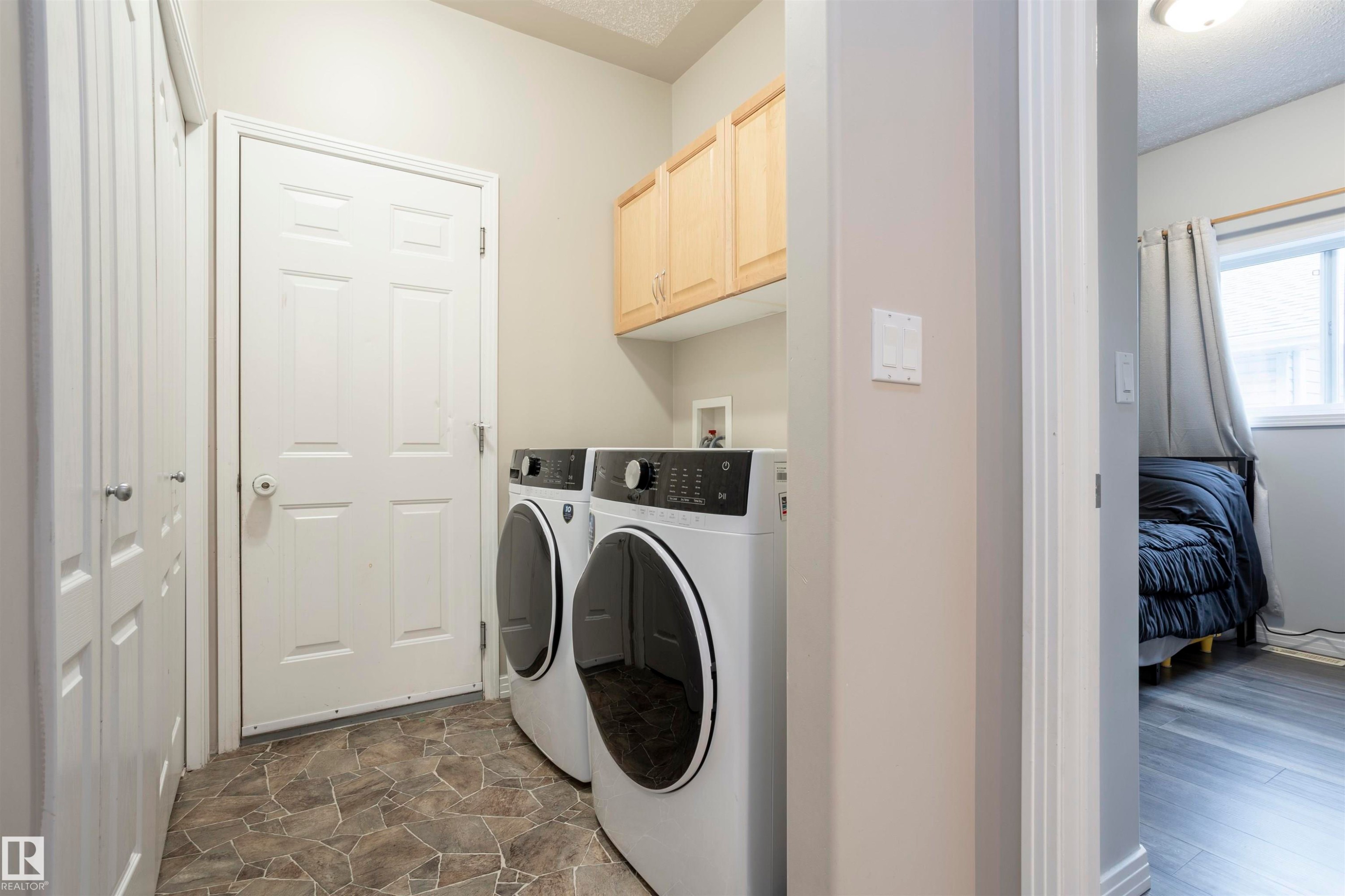 Dedicated laundry area featuring a tile-patterned floor, overhead cabinetry, and two bi-fold closet doors - 1441 Highwood Boulevard, Devon, AB
