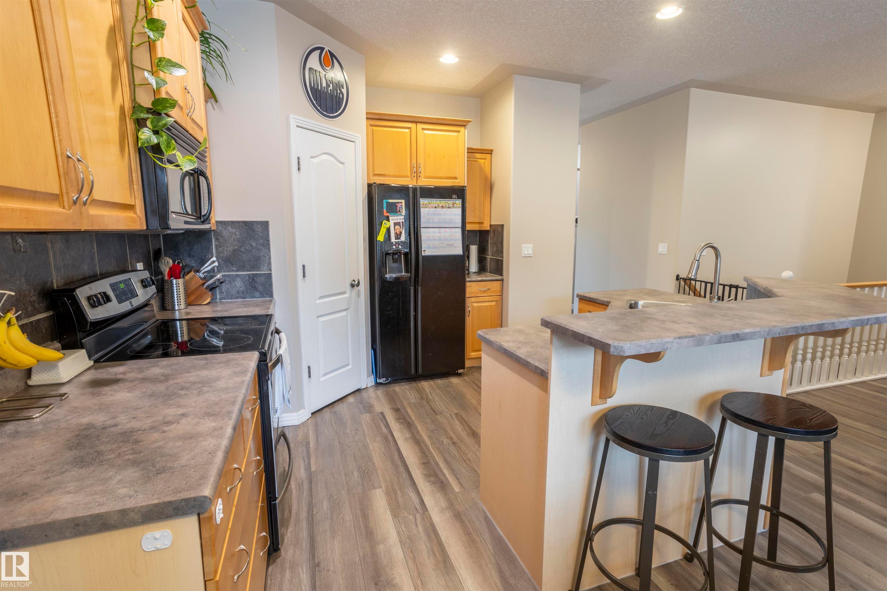 Functional kitchen featuring light wood cabinetry, dark stone-look countertops, a black electric range, and a black French door refrigerator - 1441 Highwood Boulevard, Devon, AB