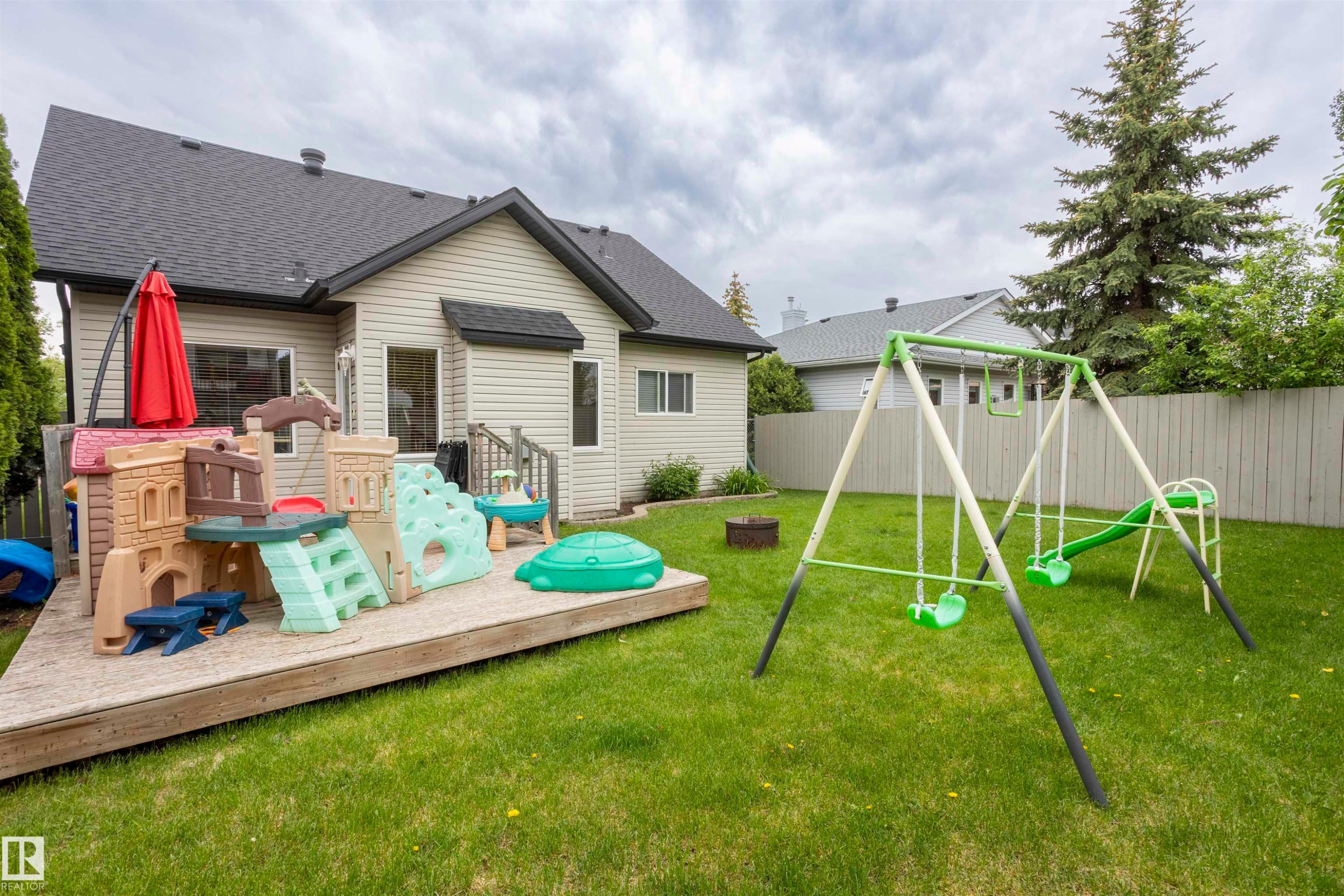 Expansive backyard featuring a manicured lawn, a raised wooden deck, tan siding, and a dark shingle roof - 1441 Highwood Boulevard, Devon, AB