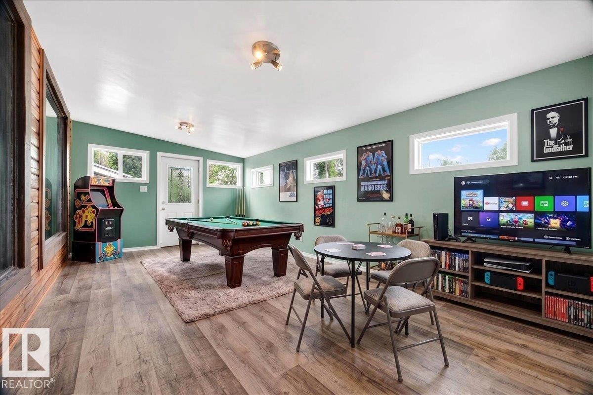 Entertainment room featuring wood-finish flooring, a vaulted ceiling, multiple windows, and a built-in media console - 140 50047 Rge Rd 244, Rural Leduc County, AB