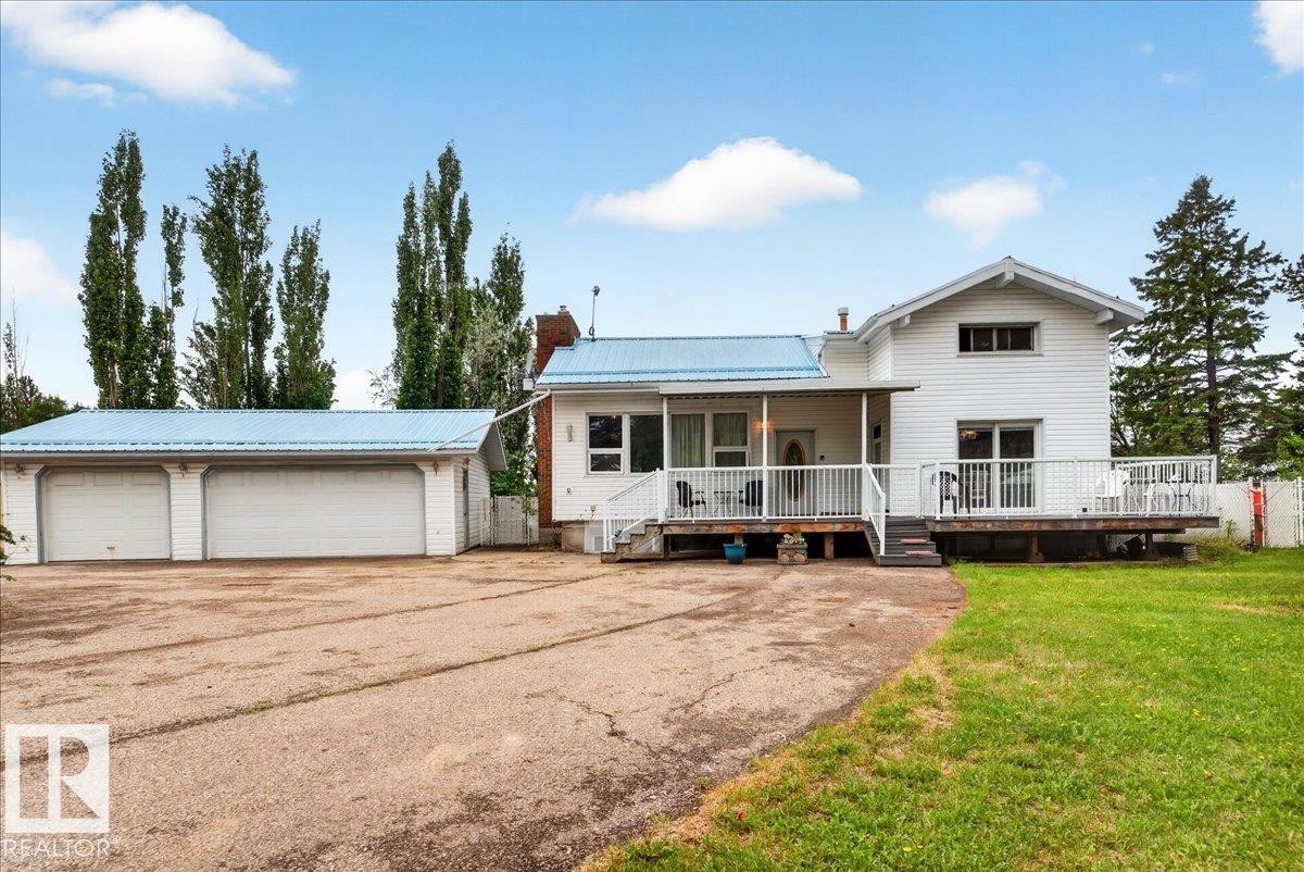 White exterior with a light blue metal roof, featuring a multi-car garage, expansive driveway, and a large deck with white railings - 140 50047 Rge Rd 244, Rural Leduc County, AB