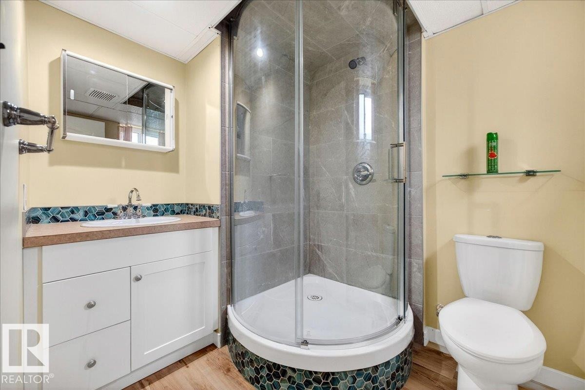 Full bathroom featuring a corner shower with glass enclosure, white vanity with integrated sink, teal mosaic tile backsplash, and wood-finish flooring - 140 50047 Rge Rd 244, Rural Leduc County, AB