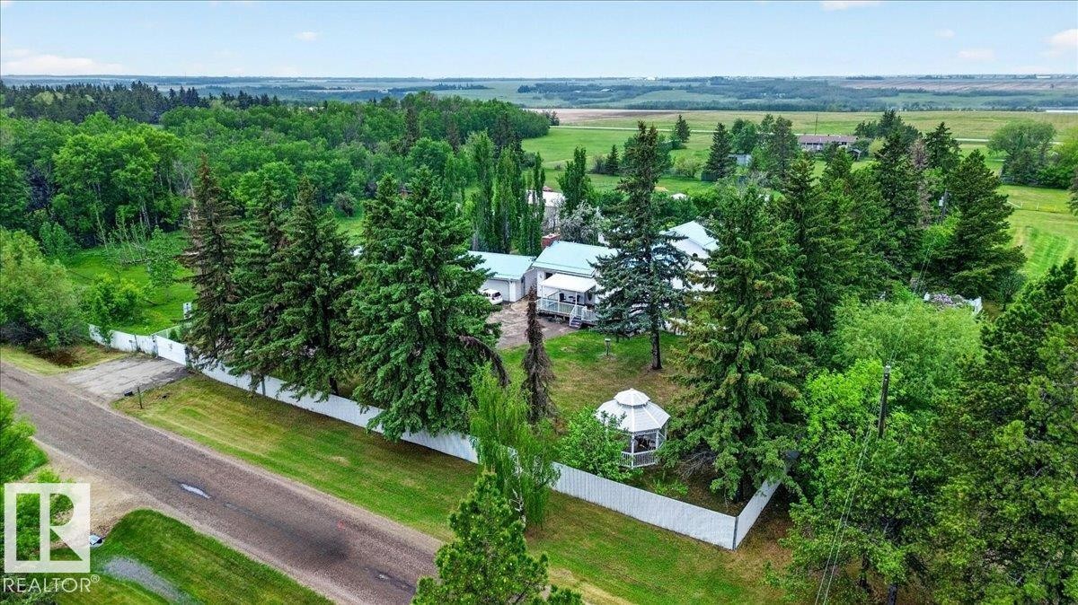 Expansive property featuring a white privacy fence, mature evergreen trees, a white outdoor gazebo, and distant cultivated fields - 140 50047 Rge Rd 244, Rural Leduc County, AB
