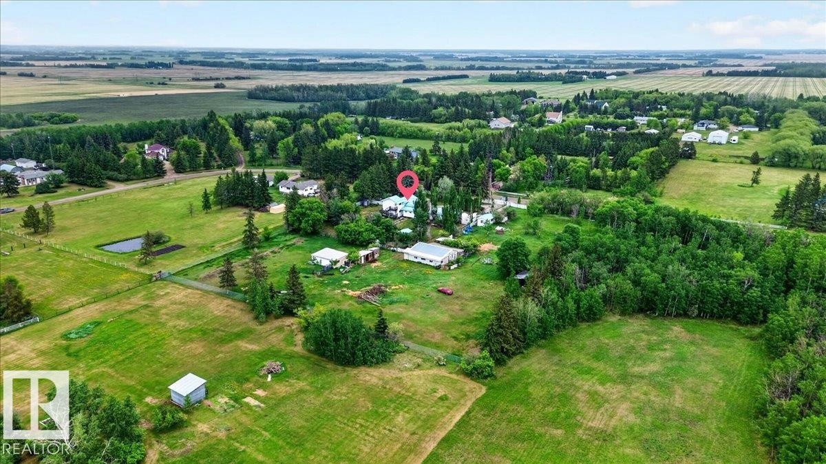 Aerial view of a rural landscape featuring expansive green fields, scattered residential structures, and mature tree lines - 140 50047 Rge Rd 244, Rural Leduc County, AB