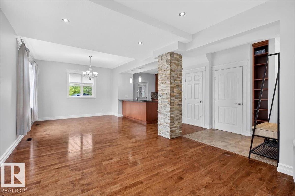 Spacious room featuring wood-finish flooring, a stone-clad structural column, recessed lighting, and a chandelier - 10958 88 Avenue, Edmonton, AB