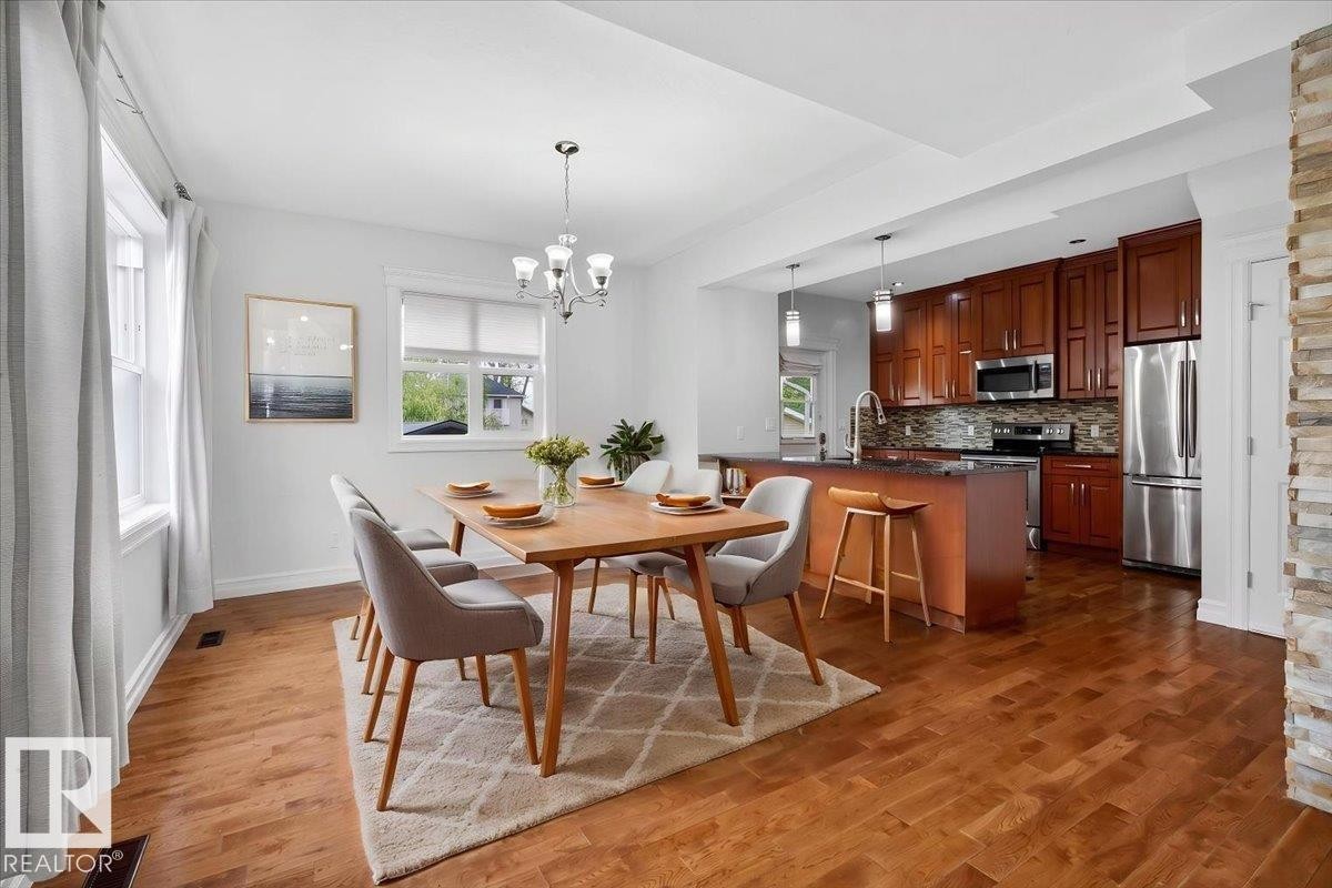 Open-concept dining area featuring wood-finish flooring, a contemporary chandelier, and ample natural light from multiple windows - 10958 88 Avenue, Edmonton, AB