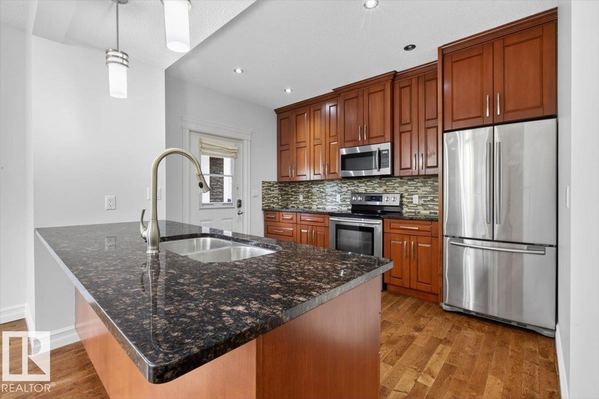 Kitchen island with dark speckled countertop and undermount double basin sink, brushed nickel gooseneck faucet, and two pendant lights - 10958 88 Avenue, Edmonton, AB