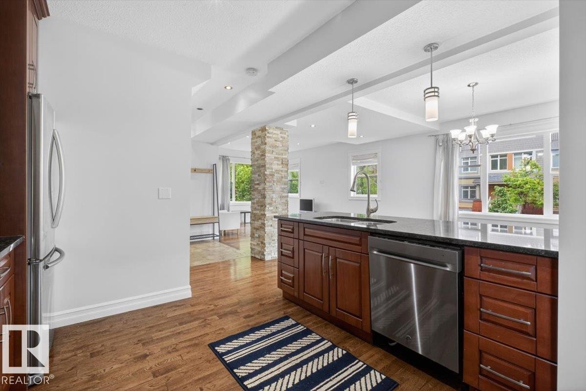 Kitchen featuring wood-finish flooring, dark wood cabinetry, a dark countertop, a stainless steel dishwasher, and a stainless steel refrigerator - 10958 88 Avenue, Edmonton, AB