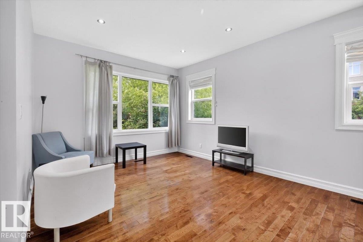 Spacious room featuring wood-finish flooring, recessed ceiling lighting, multiple windows with white trim, and light gray wall finishes - 10958 88 Avenue, Edmonton, AB