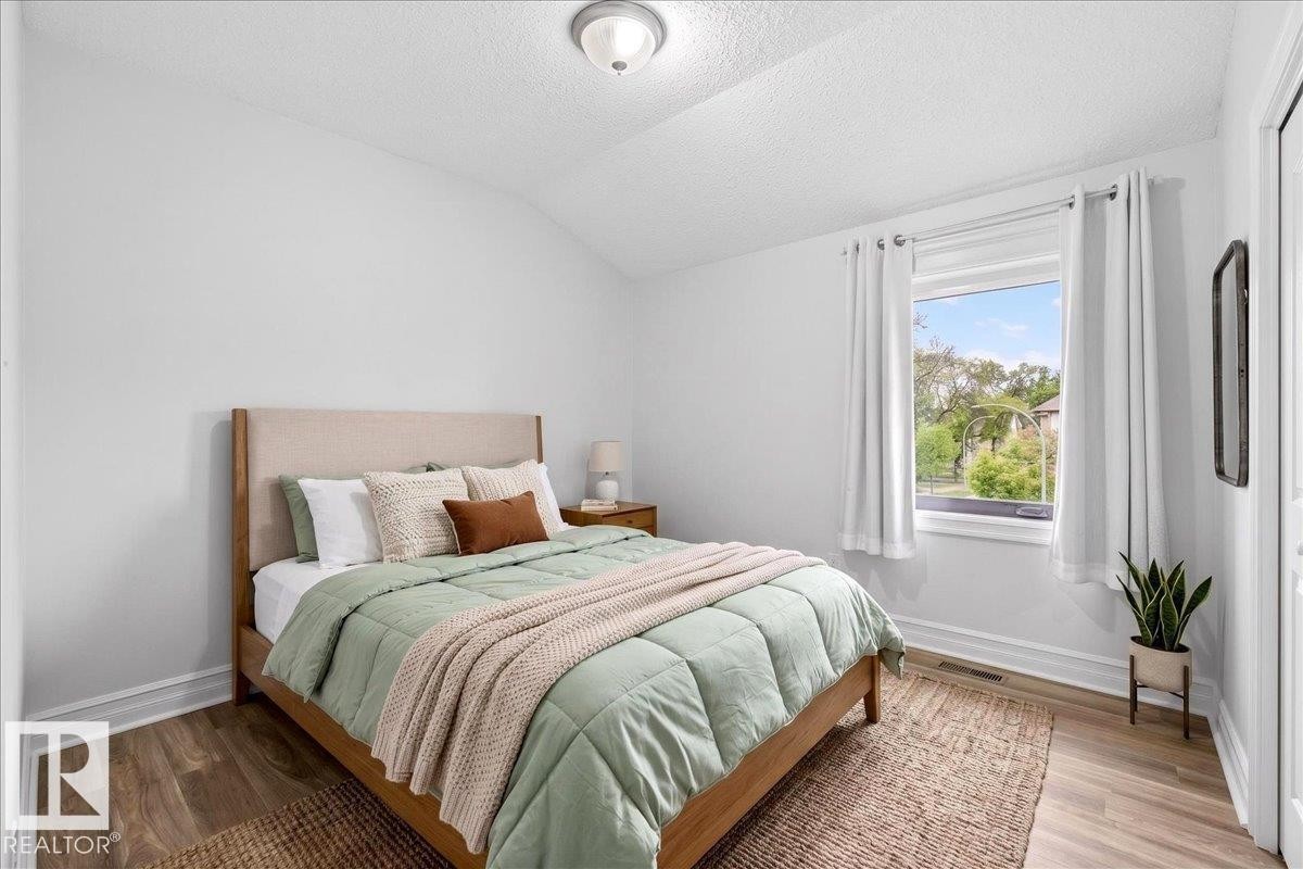 Bright bedroom featuring light-toned walls, wood-finish flooring, and white trim - 10958 88 Avenue, Edmonton, AB