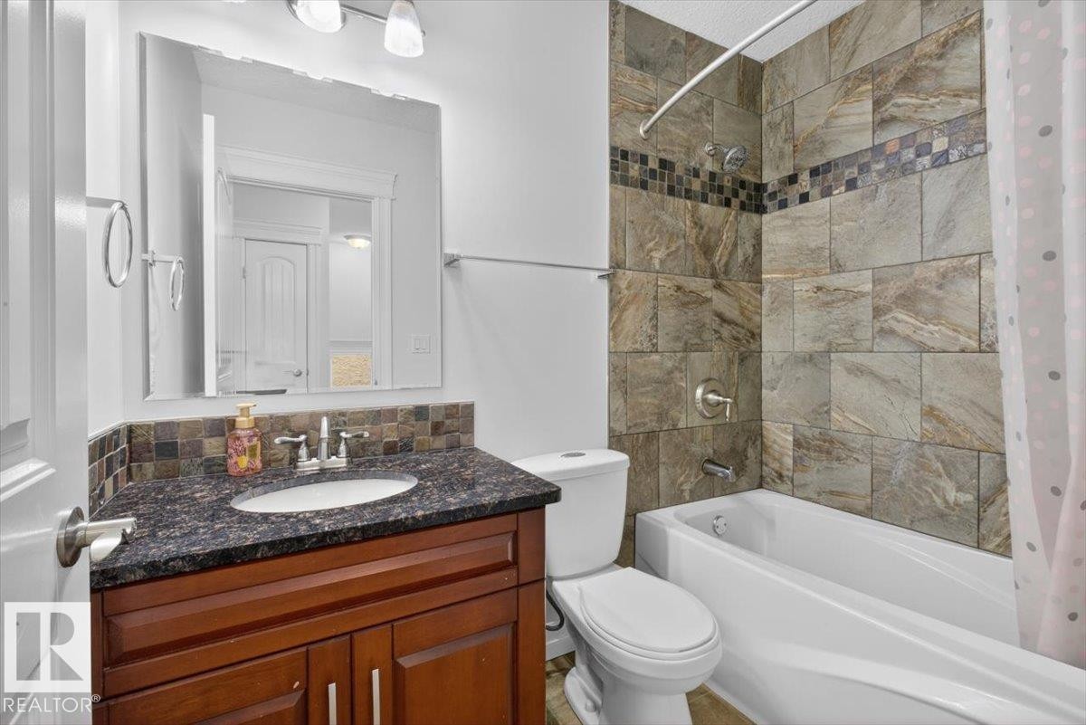 Bathroom featuring a dark wood-finish vanity with an undermount sink, a dark speckled countertop, and a tiled backsplash - 10958 88 Avenue, Edmonton, AB