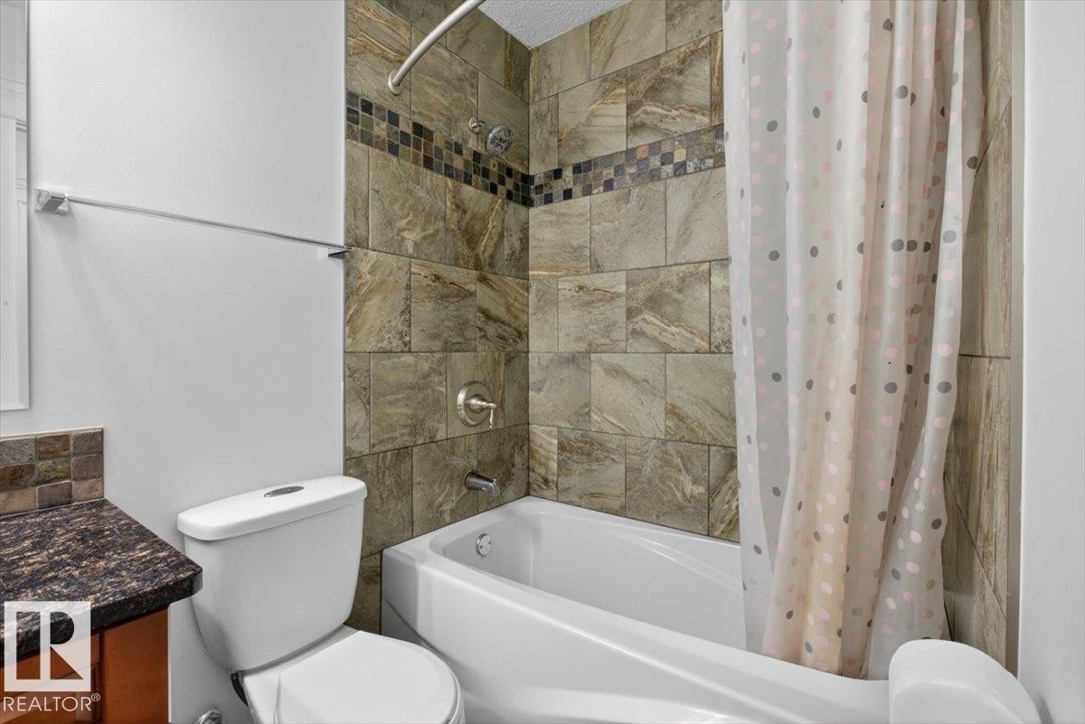 Bathroom featuring a bathtub with a tiled surround, a mosaic accent band, and a shower head with an arched shower rod - 10958 88 Avenue, Edmonton, AB