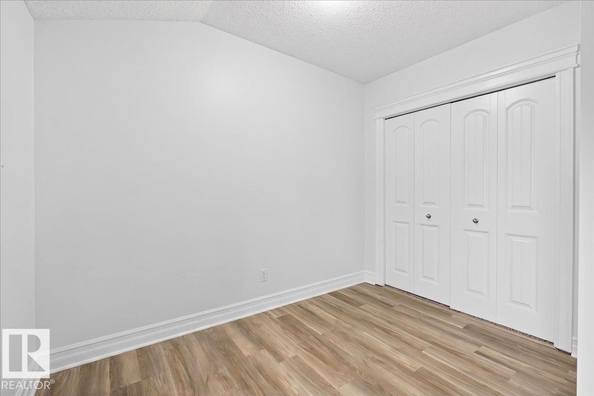 Room featuring wood-finish flooring, white walls, and a bi-fold closet with decorative trim - 10958 88 Avenue, Edmonton, AB