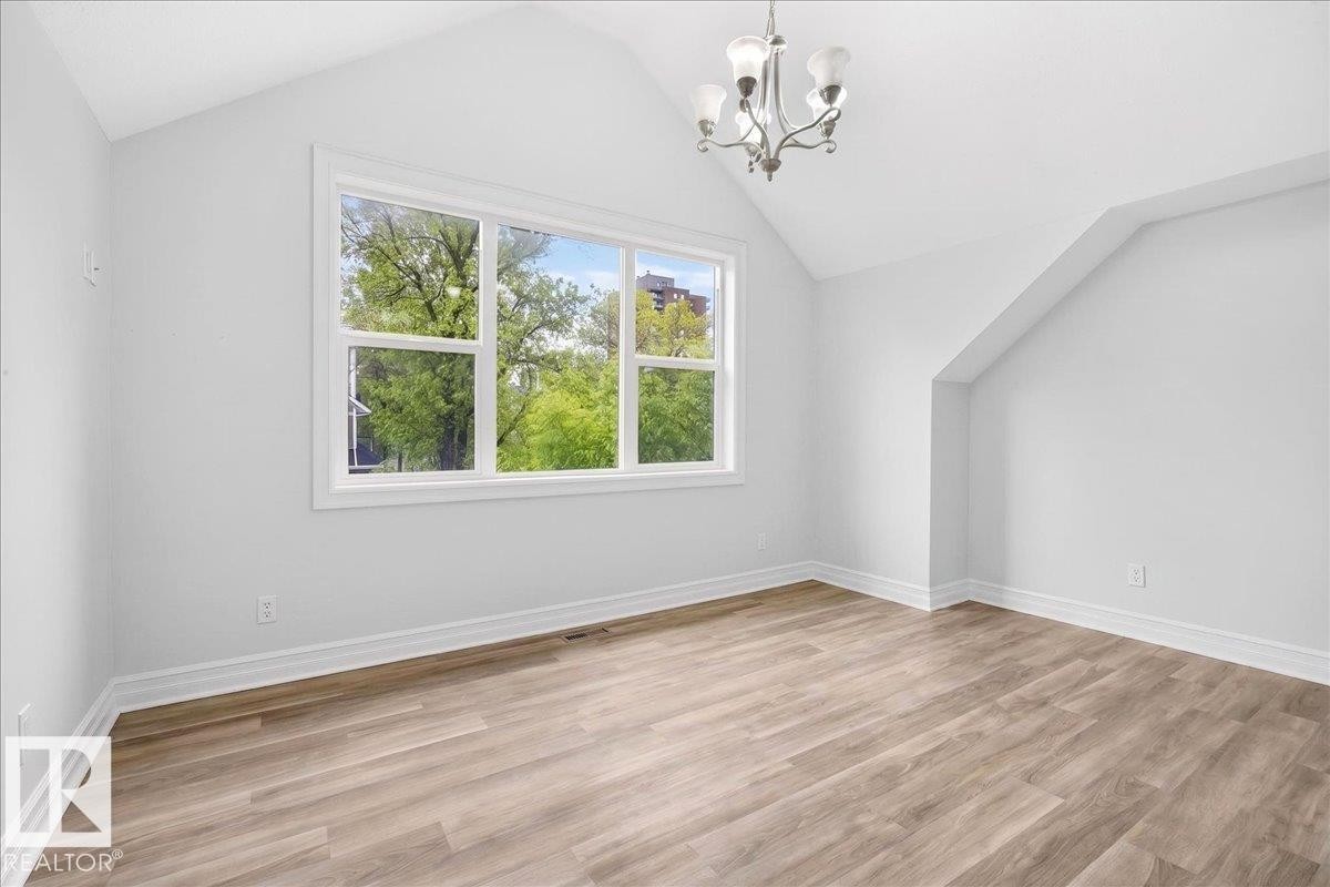 Vaulted ceiling room featuring a large multi-pane window, wood-finish flooring, white baseboards, and a contemporary chandelier - 10958 88 Avenue, Edmonton, AB