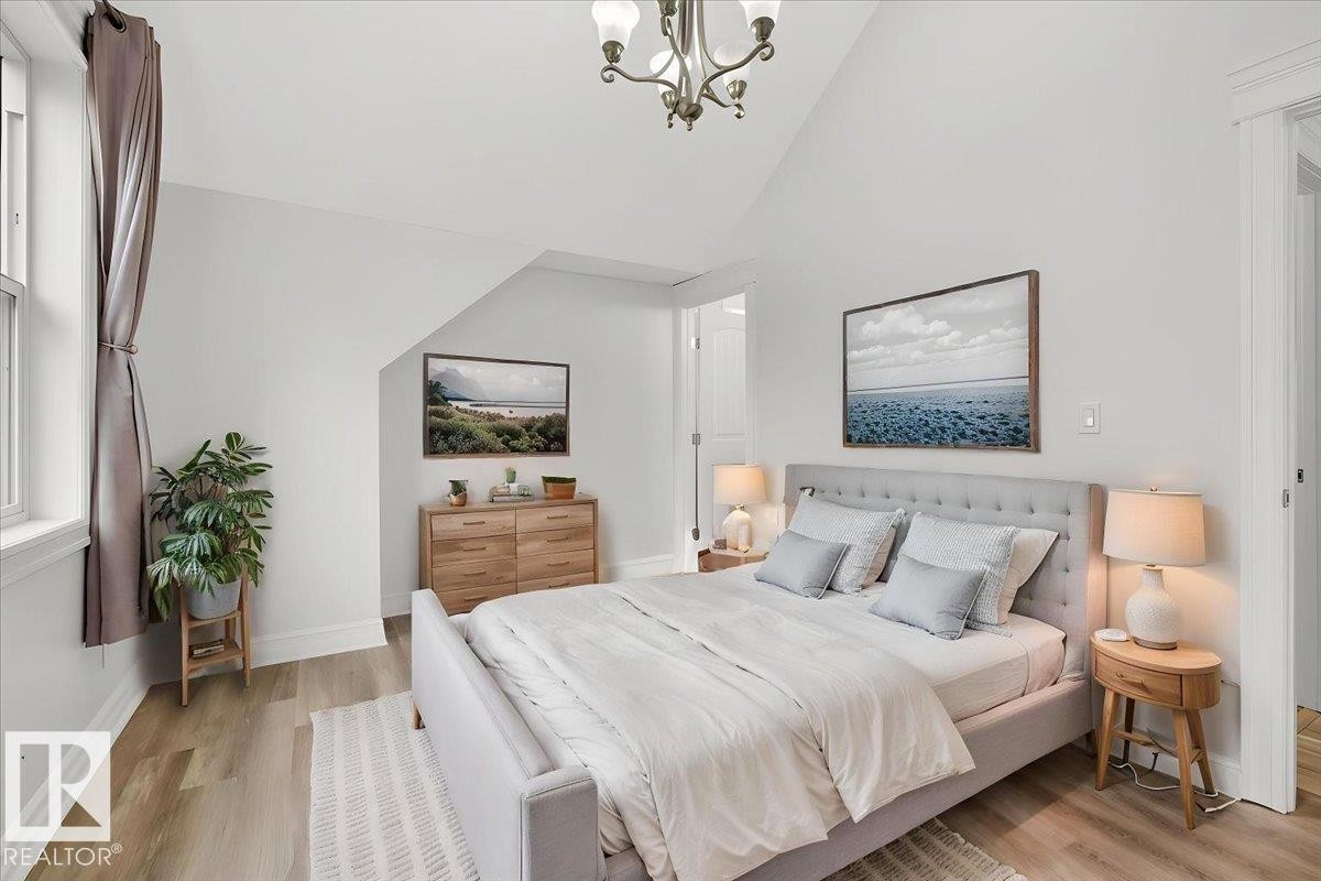 Vaulted ceiling bedroom with wood-finish flooring, a window with trim, a built-in closet with a solid door, and a chandelier - 10958 88 Avenue, Edmonton, AB