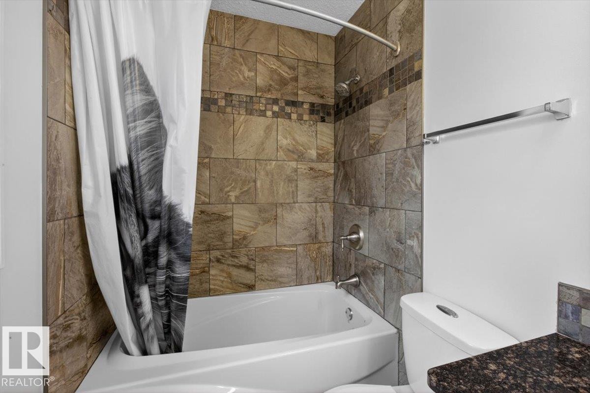 Bathtub and shower combination featuring earth-toned wall tiling, a decorative mosaic accent band, and brushed nickel fixtures - 10958 88 Avenue, Edmonton, AB