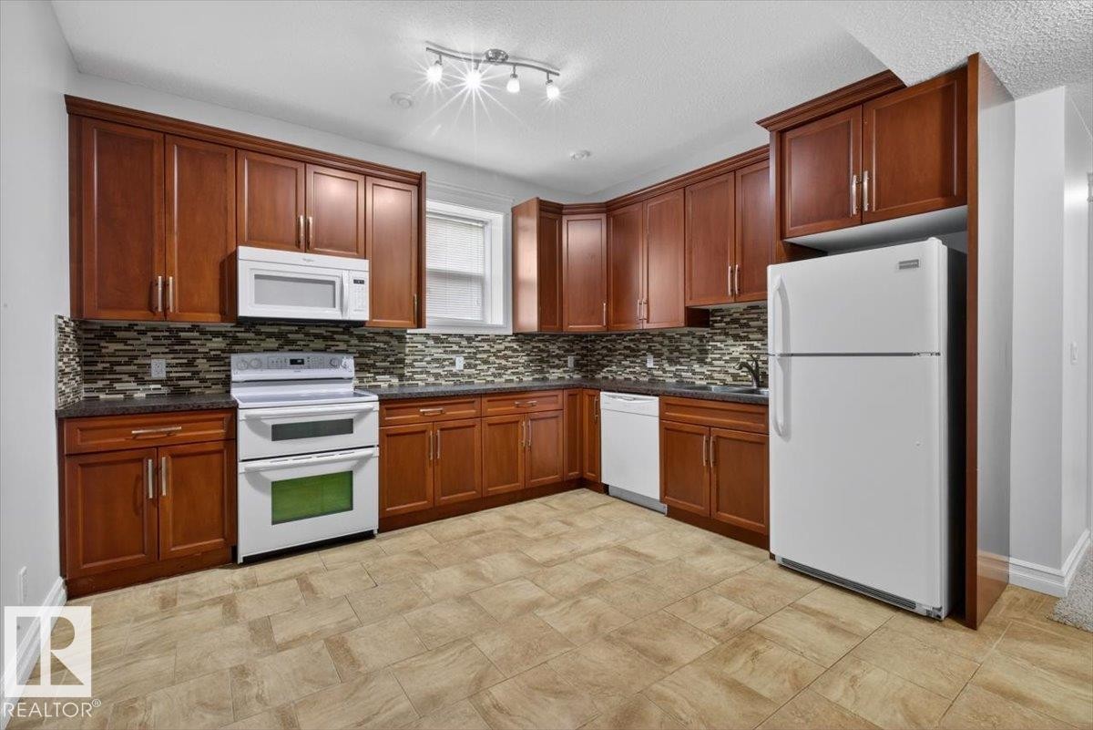 Kitchen featuring rich wood cabinetry, stone countertops, a mosaic tile backsplash, and light-toned tile flooring - 10958 88 Avenue, Edmonton, AB