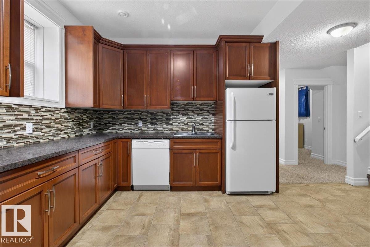 Kitchen featuring wood cabinetry, stone-finish countertops, and a mosaic tile backsplash - 10958 88 Avenue, Edmonton, AB