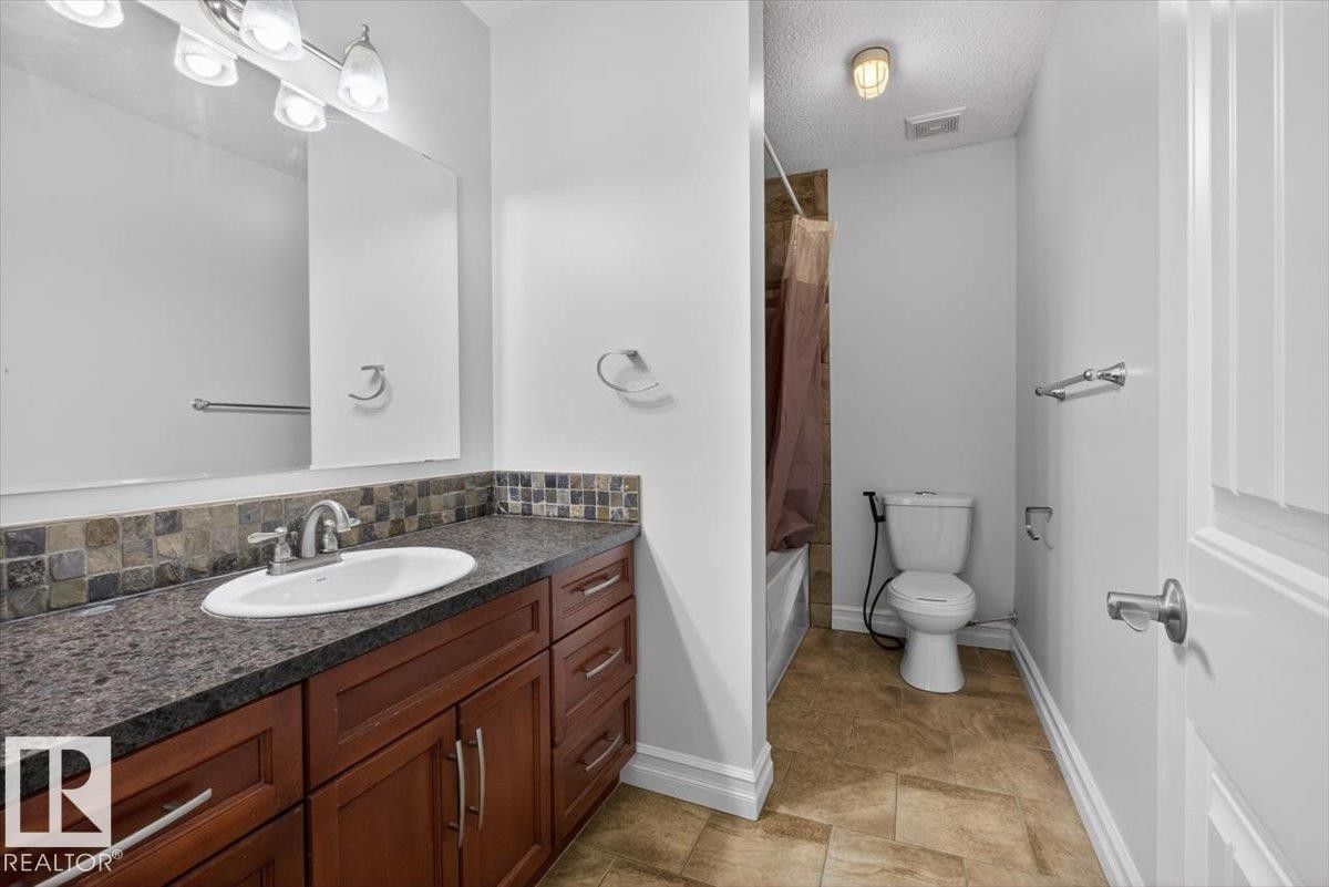 Bathroom featuring a vanity with dark countertop, undermount sink, and mosaic tile backsplash - 10958 88 Avenue, Edmonton, AB