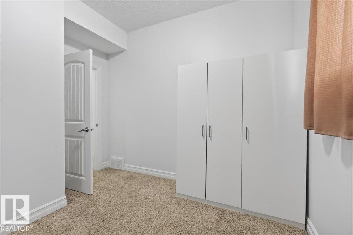 Carpeted room featuring a white paneled door, built-in white cabinetry, baseboard trim, and a window with a curtain - 10958 88 Avenue, Edmonton, AB