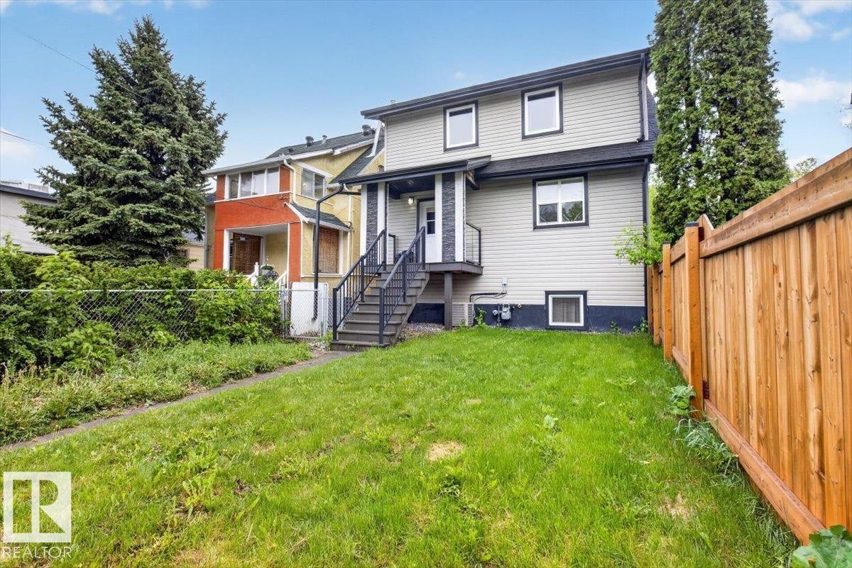 Rear exterior featuring light-colored siding, contrasting trim, a wood privacy fence, and an exterior staircase with metal railings - 10958 88 Avenue, Edmonton, AB