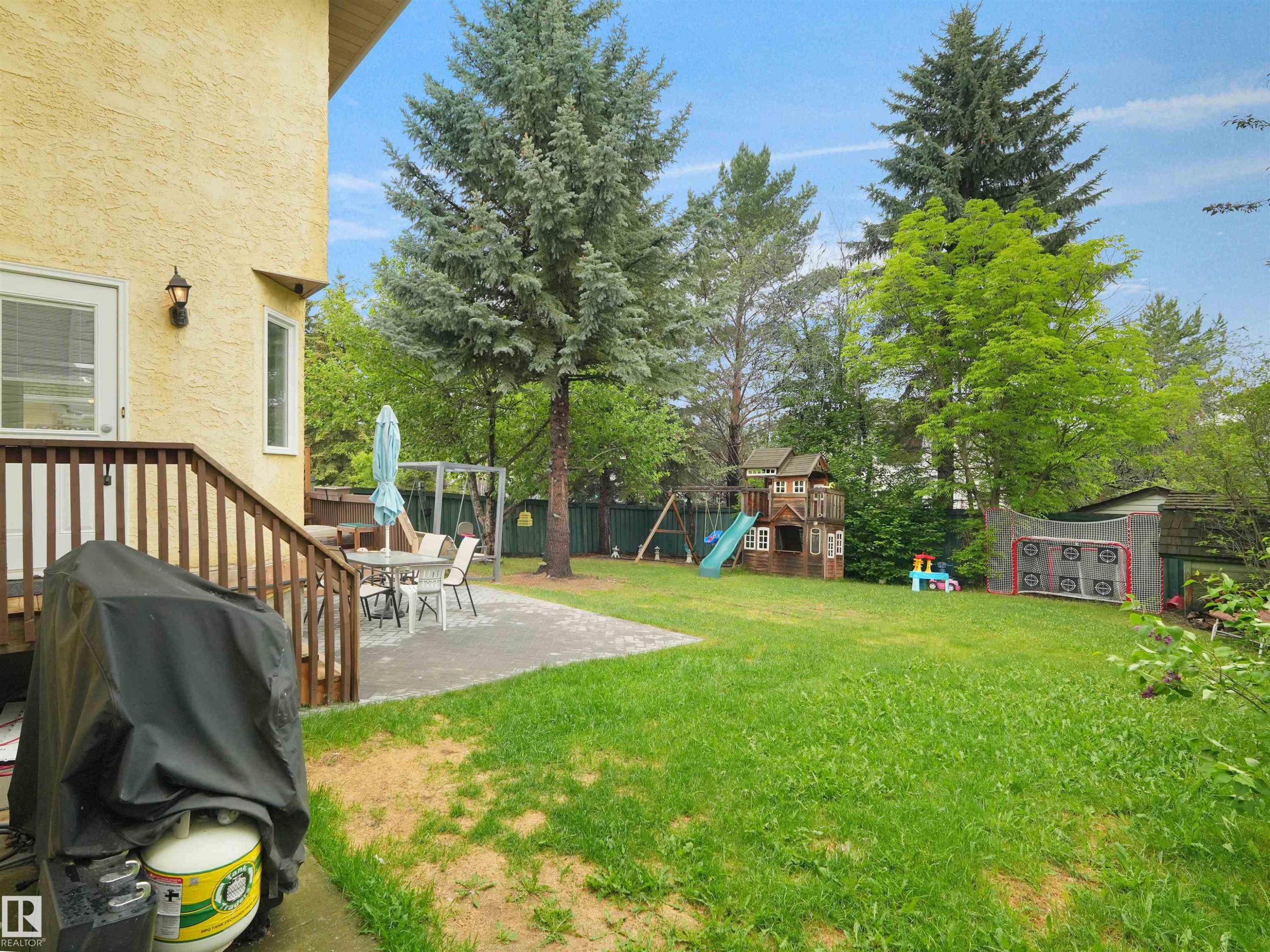 Generous backyard featuring a wooden deck, a paved patio, and a vast lawn area - 208 Ferguson Place, Edmonton, AB
