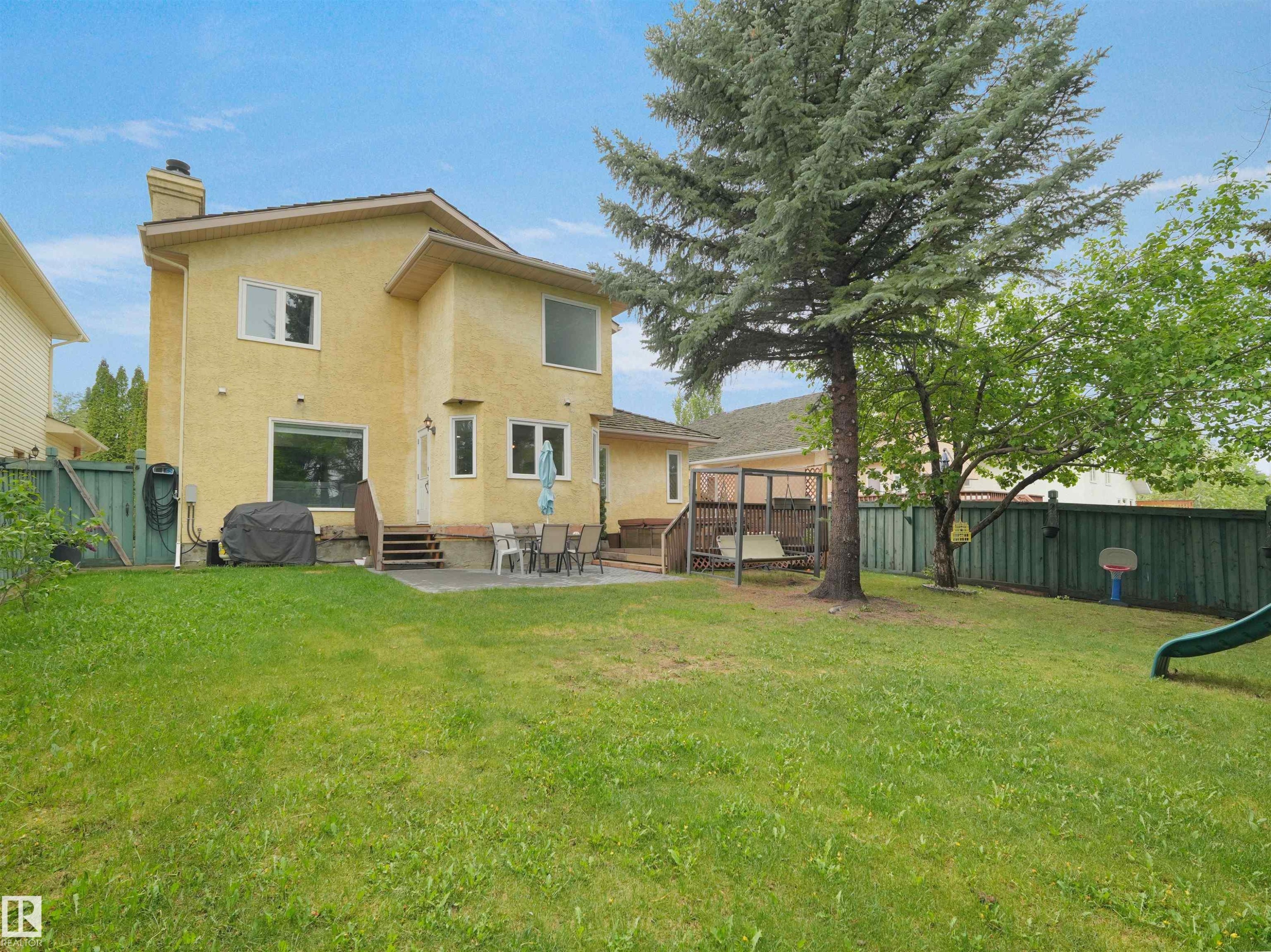 Expansive rear yard featuring a large evergreen tree, mature deciduous tree, and a green wood fence - 208 Ferguson Place, Edmonton, AB