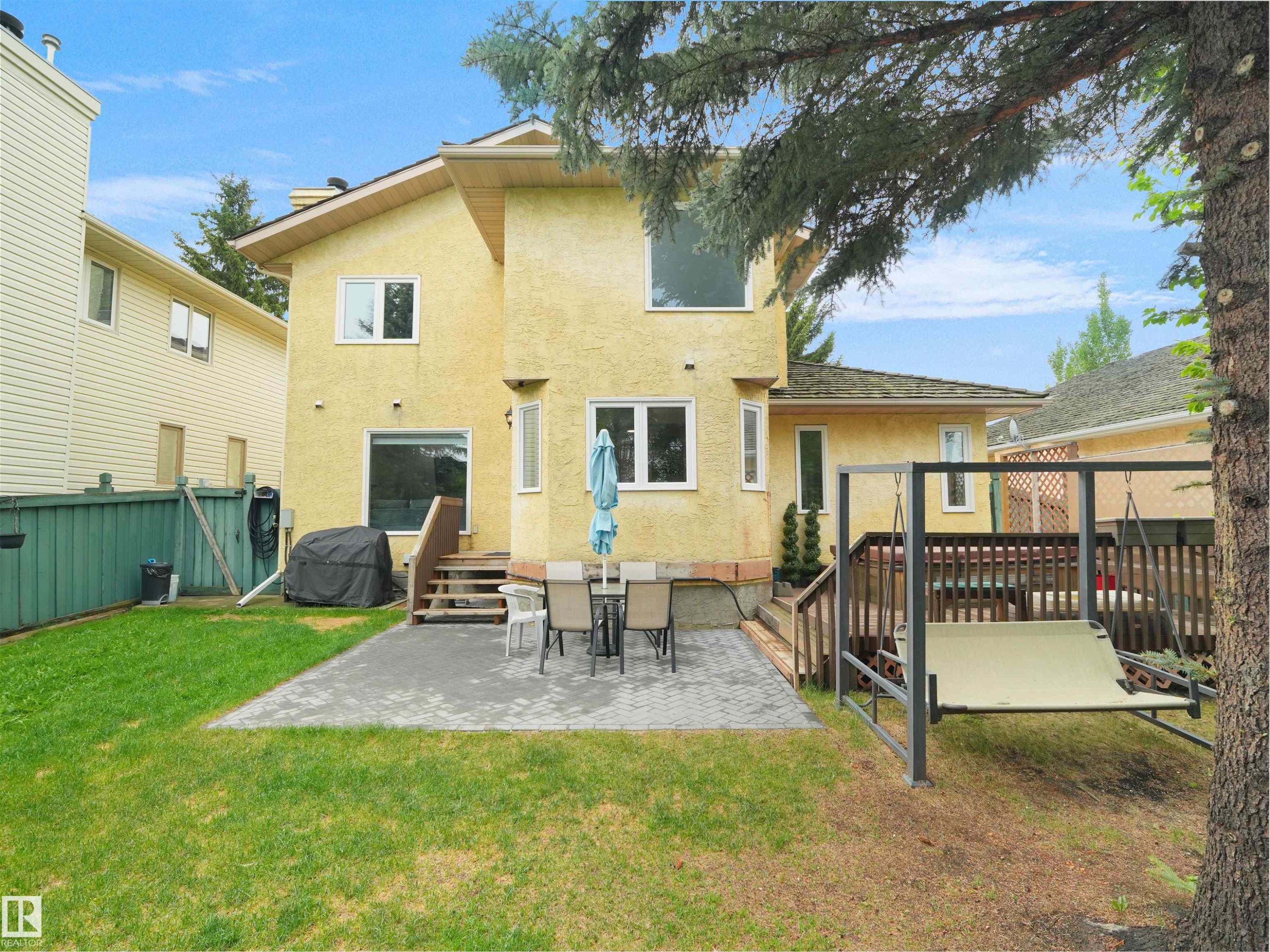 Expansive backyard featuring a manicured lawn, a large patio area with paver stones, and a wooden deck with railing - 208 Ferguson Place, Edmonton, AB