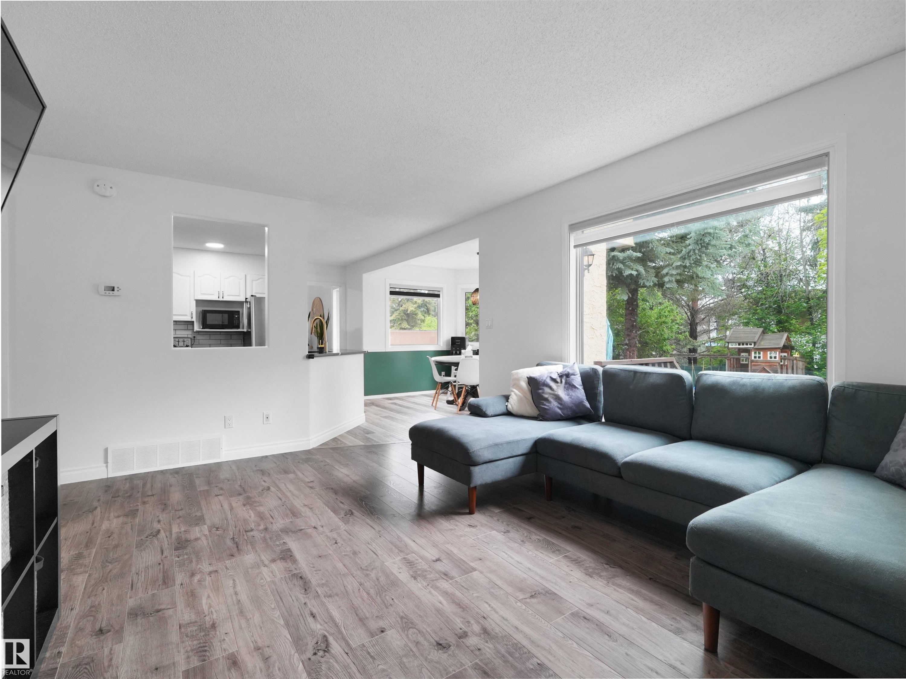 Spacious living area featuring wood-finish flooring, a large picture window, and white walls - 208 Ferguson Place, Edmonton, AB