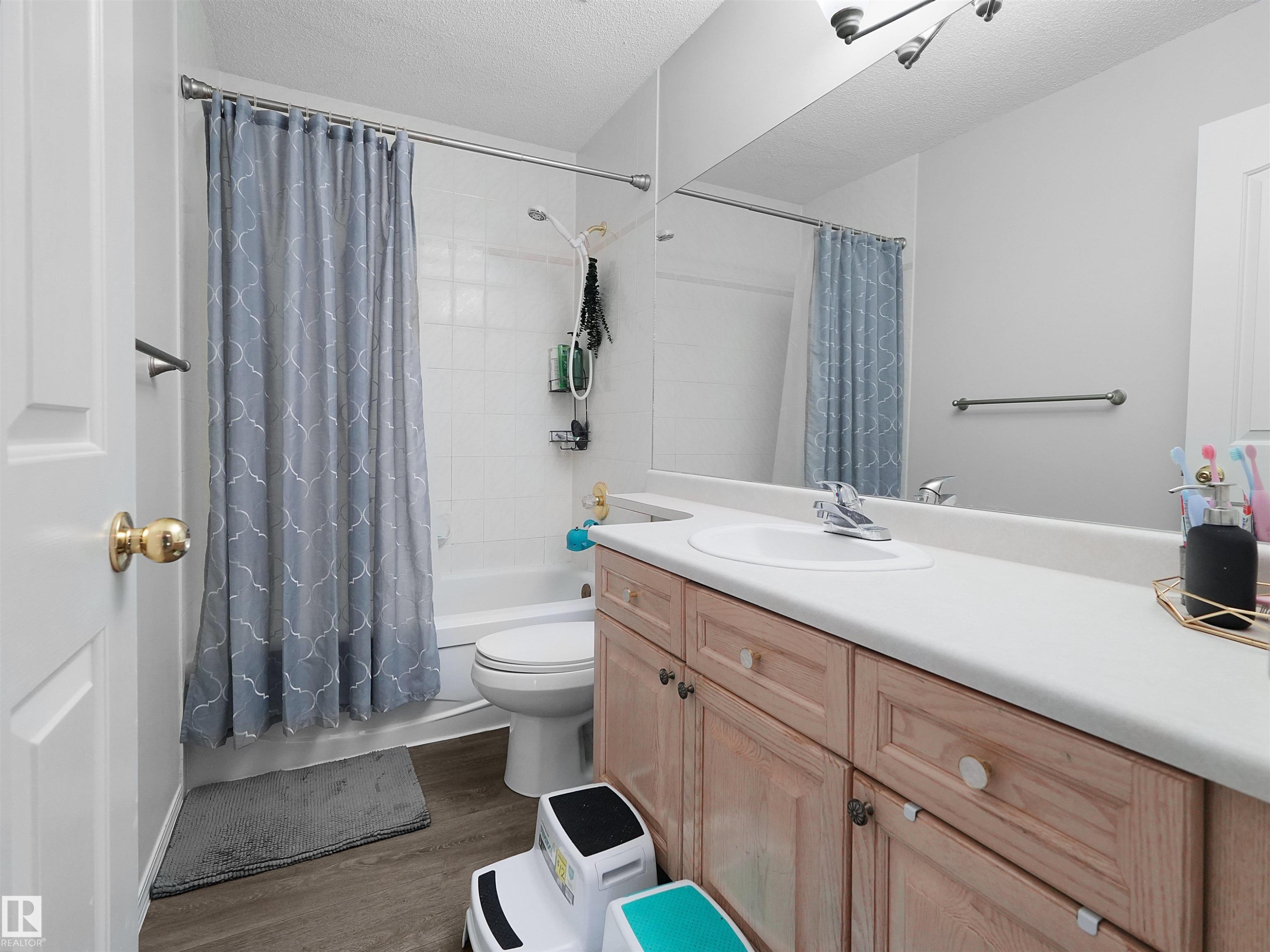 Full bathroom featuring a single vanity with wood-finish cabinetry, a white countertop with integrated sink, and a combination tub and shower with white tiled surround - 208 Ferguson Place, Edmonton, AB