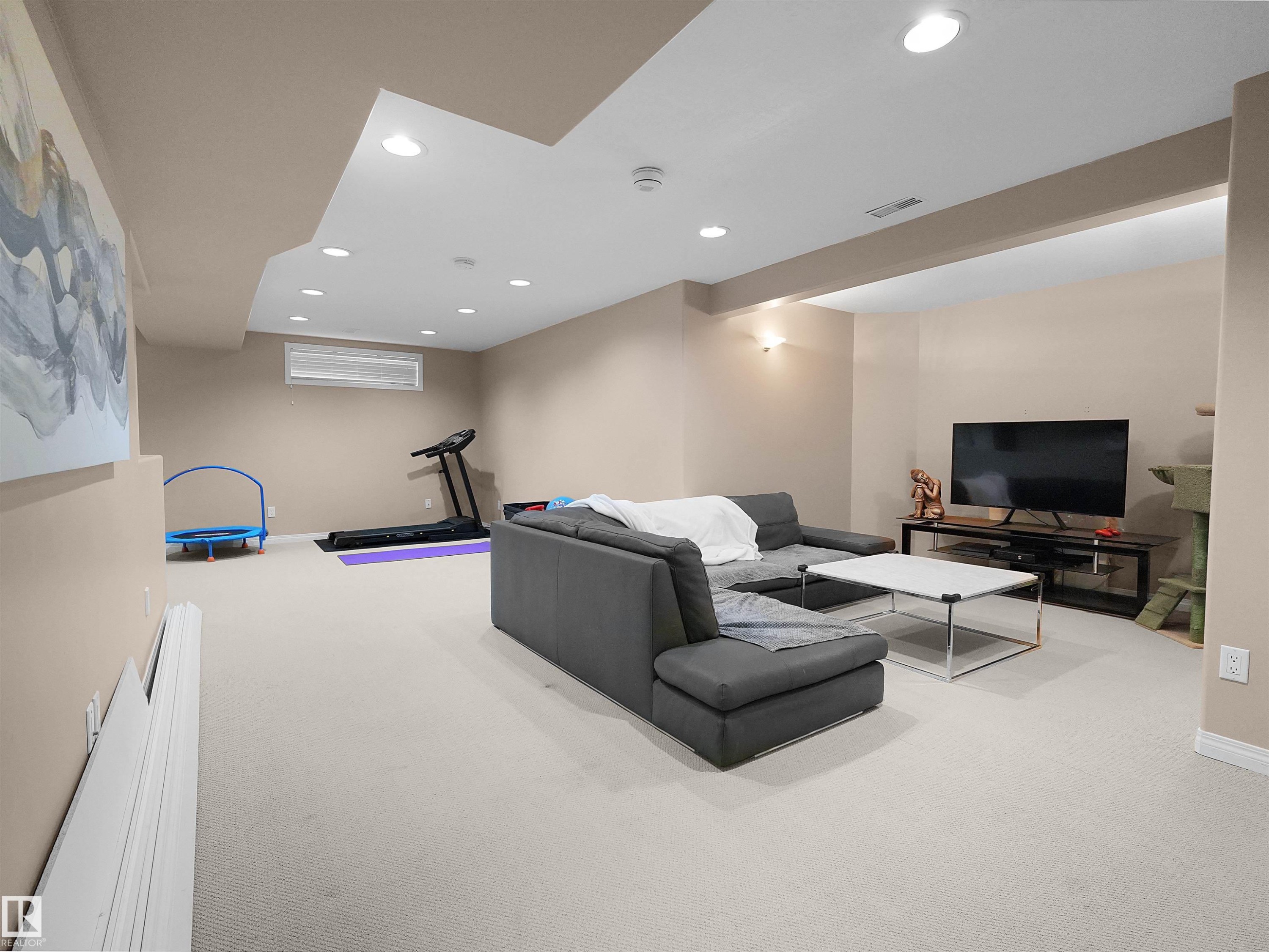 Spacious room featuring neutral carpeting, recessed lighting, and a drop ceiling with integrated fixtures - 208 Ferguson Place, Edmonton, AB