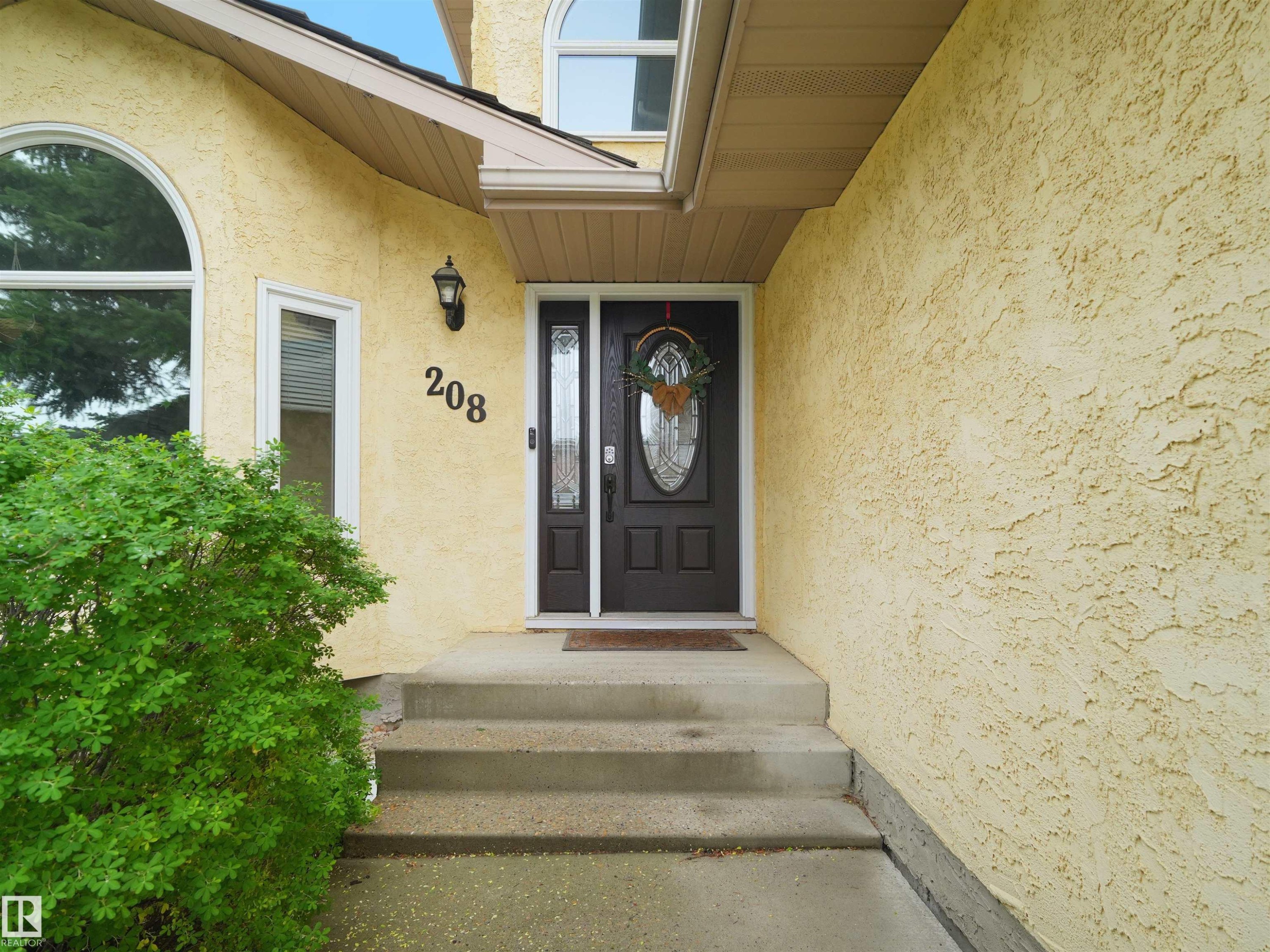 Inviting entryway featuring a dark wood-finish door with decorative glass inserts, a complementary sidelight, and an exterior wall light fixture - 208 Ferguson Place, Edmonton, AB