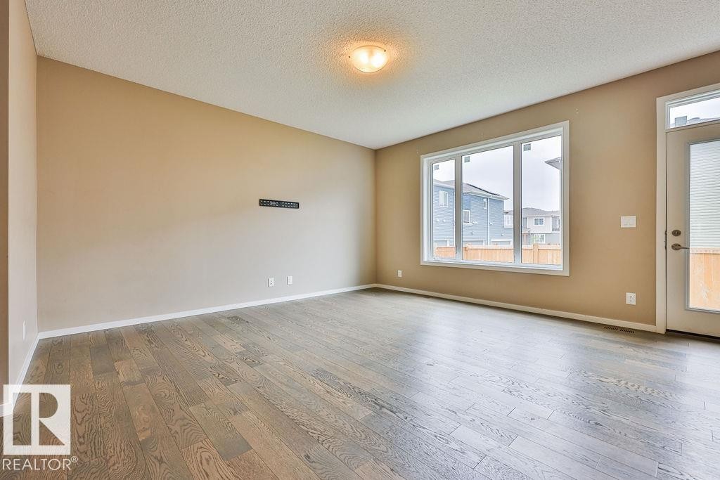 Spacious room featuring wood-finish flooring, a large window, and a glass-paneled door - 2031 207 Street, Edmonton, AB