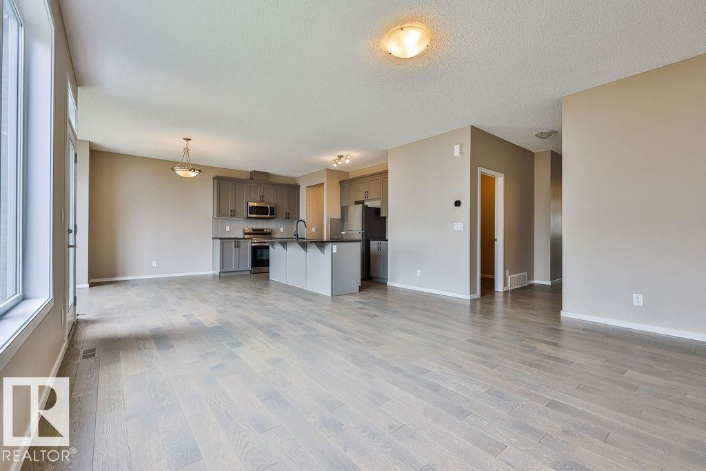 Open-concept living space featuring wood-finish flooring, a modern kitchen with gray cabinetry and dark countertops, stainless steel appliances, and abundant natural light from large windows - 2031 207 Street, Edmonton, AB