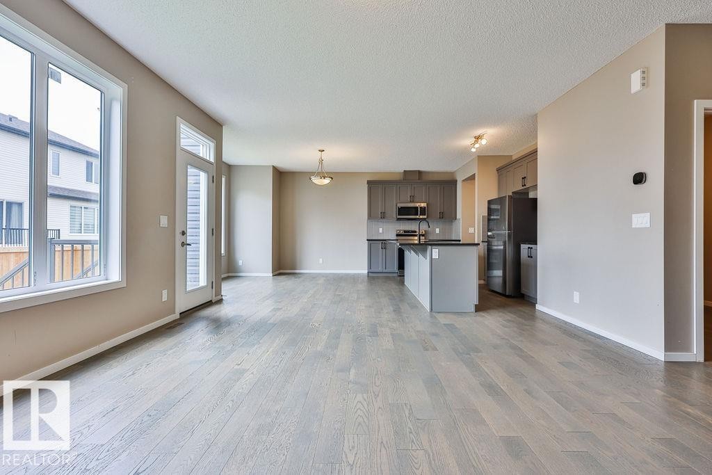 Expansive open-concept living area featuring wood-finish flooring, large windows, and a glass-paneled exterior door - 2031 207 Street, Edmonton, AB
