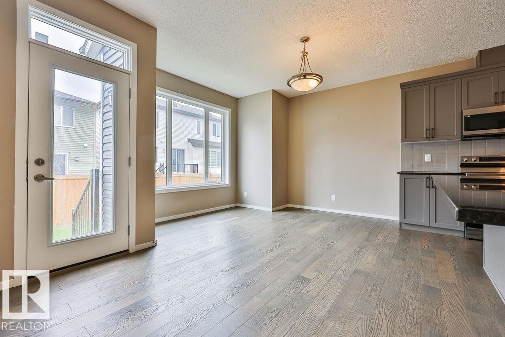 Open-concept living space featuring wood-finish flooring, a full-light exterior door, and a multi-pane window - 2031 207 Street, Edmonton, AB