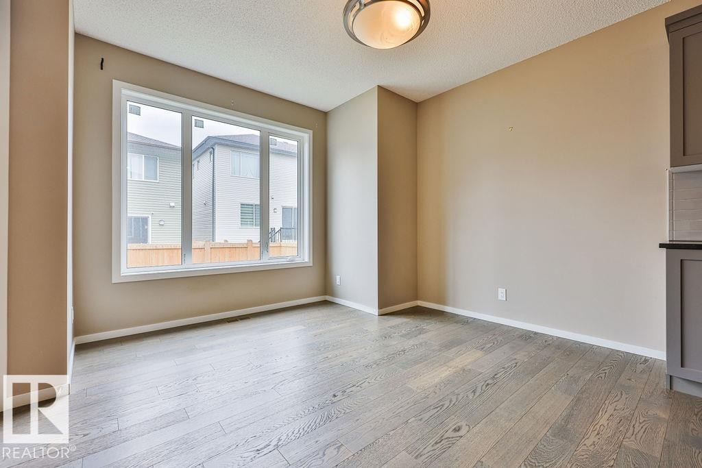 Spacious interior featuring wide-plank wood-finish flooring, a large multi-pane window, neutral wall tones, and a semi-flush mount ceiling light - 2031 207 Street, Edmonton, AB