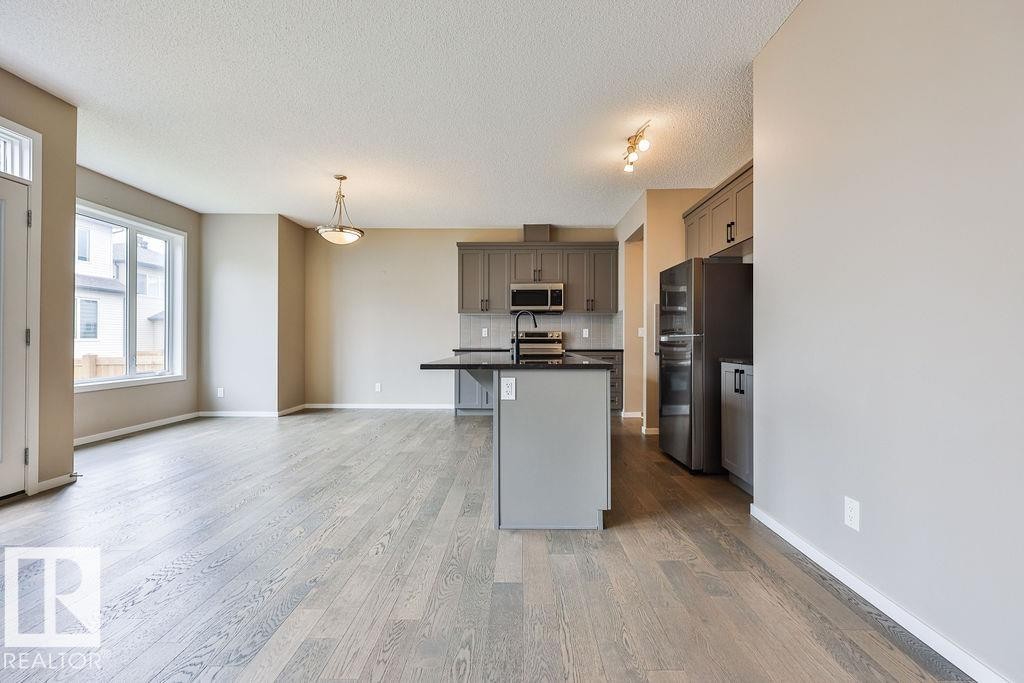 Open-concept living area with wood-finish flooring, a large window, and a kitchen featuring gray cabinetry, dark countertops, and stainless steel appliances - 2031 207 Street, Edmonton, AB