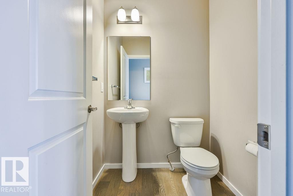 Powder room featuring a pedestal sink with chrome faucet, a rectangular wall-mounted mirror, and a two-light vanity fixture - 2031 207 Street, Edmonton, AB