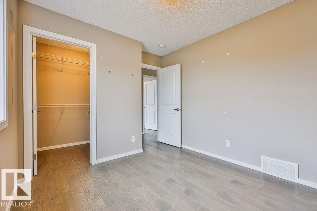 Room featuring wood-finish flooring, neutral wall paint, and a built-in closet with shelving - 2031 207 Street, Edmonton, AB