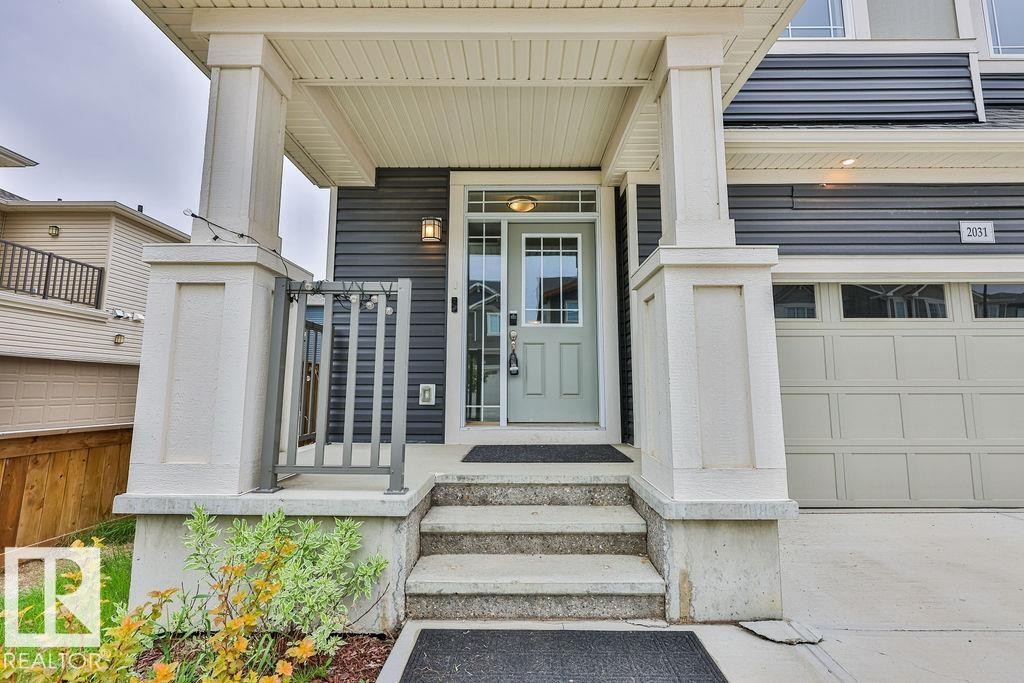 Covered front entryway featuring a light-colored door with glass inserts, concrete steps, and a metal handrail - 2031 207 Street, Edmonton, AB