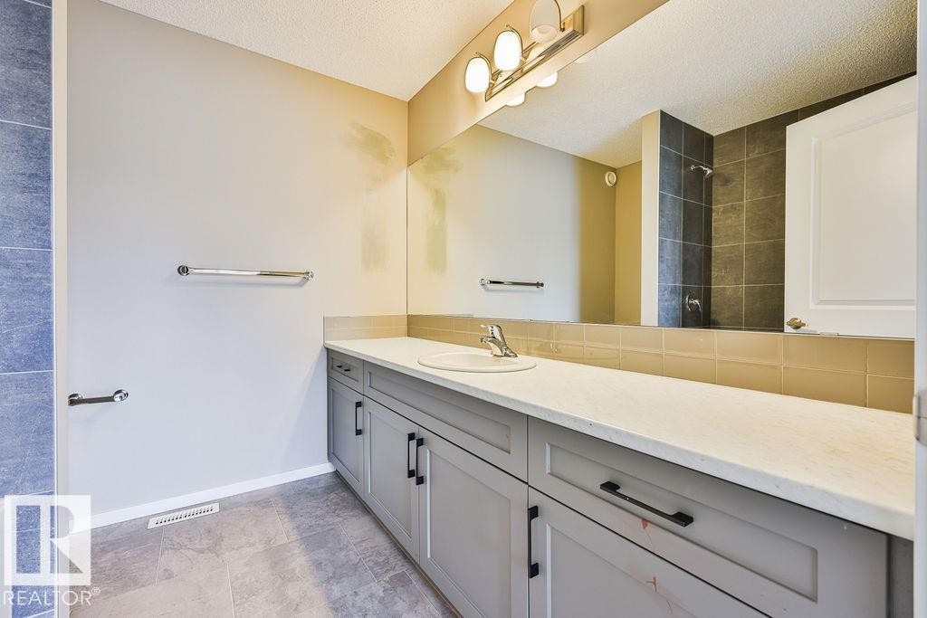Bathroom vanity featuring light gray cabinetry with black hardware, a white countertop, and a single undermount sink with a chrome faucet - 2031 207 Street, Edmonton, AB