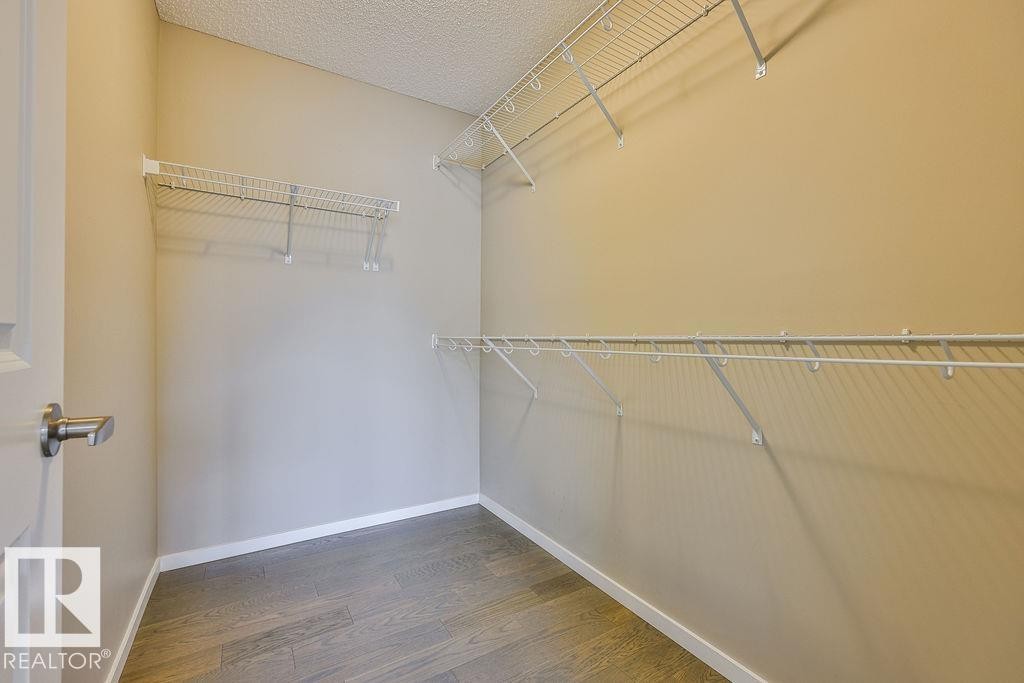 Walk-in closet featuring wood-finish flooring, neutral wall paint, white baseboards, and wire shelving with hanging rods - 2031 207 Street, Edmonton, AB