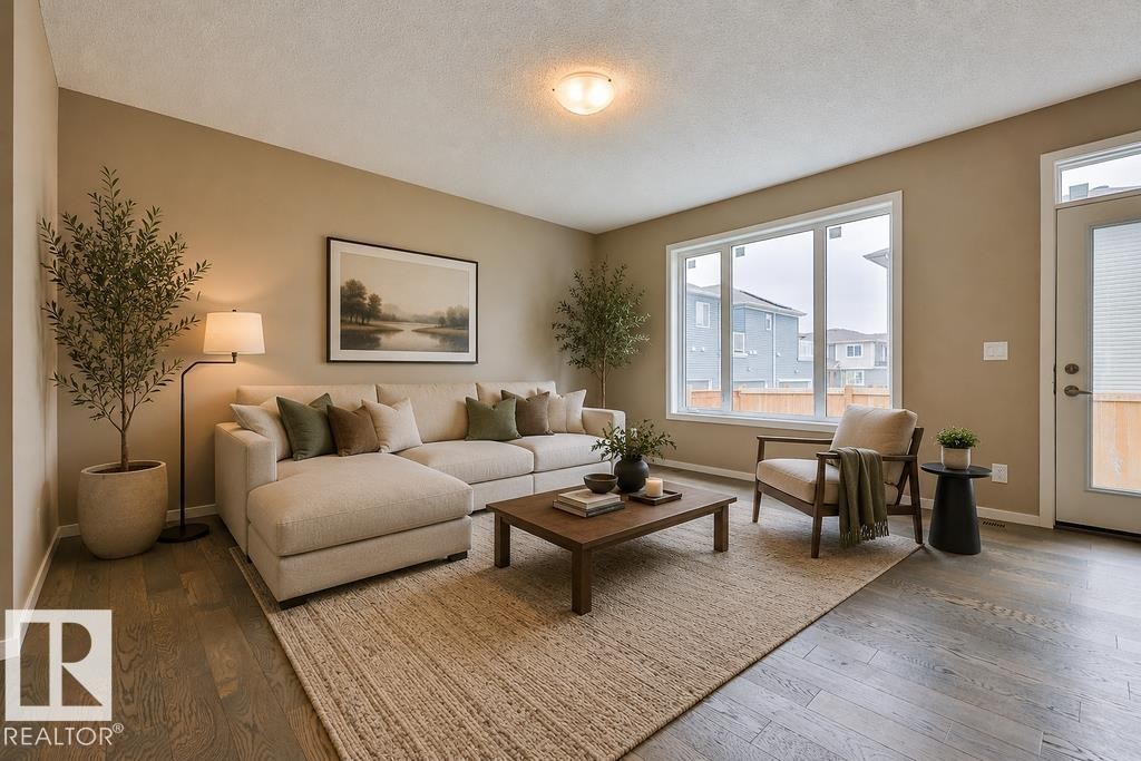 Bright living room featuring wood-finish flooring, a large multi-pane window, and a glass-paneled exterior door. Virtually Staged Photos - 2031 207 Street, Edmonton, AB